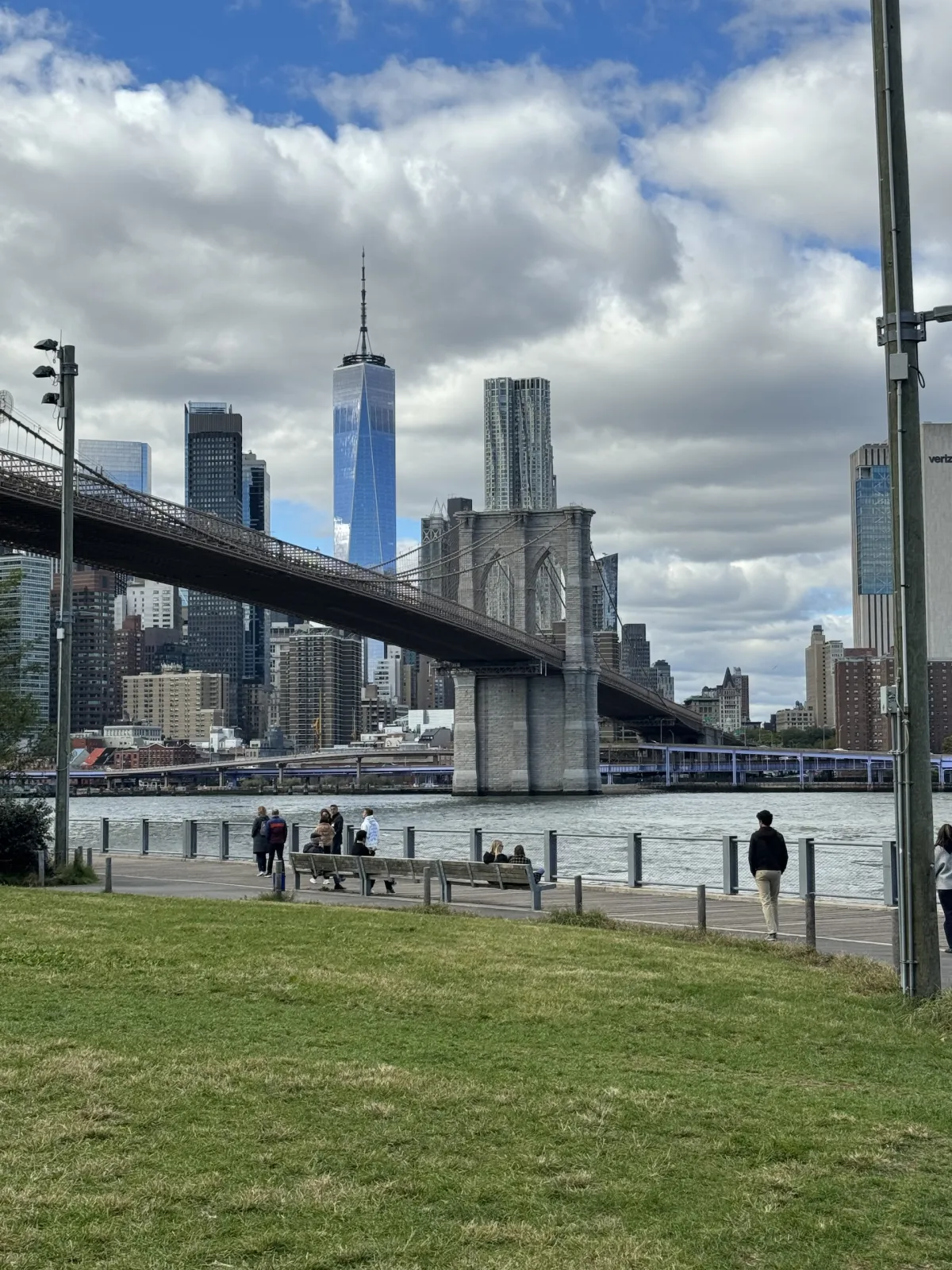 The Brooklyn Bridge seen from a riverside park, with the Manhattan skyline behind.