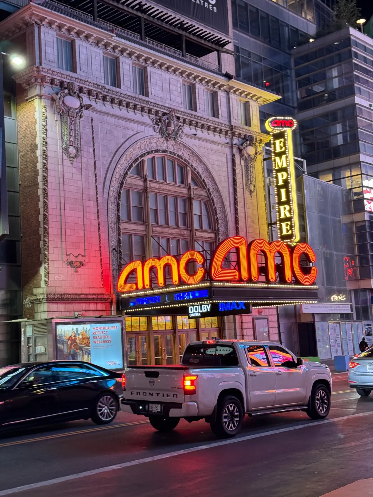The lit AMC Empire cinema frontage at night, with traffic passing in front.
