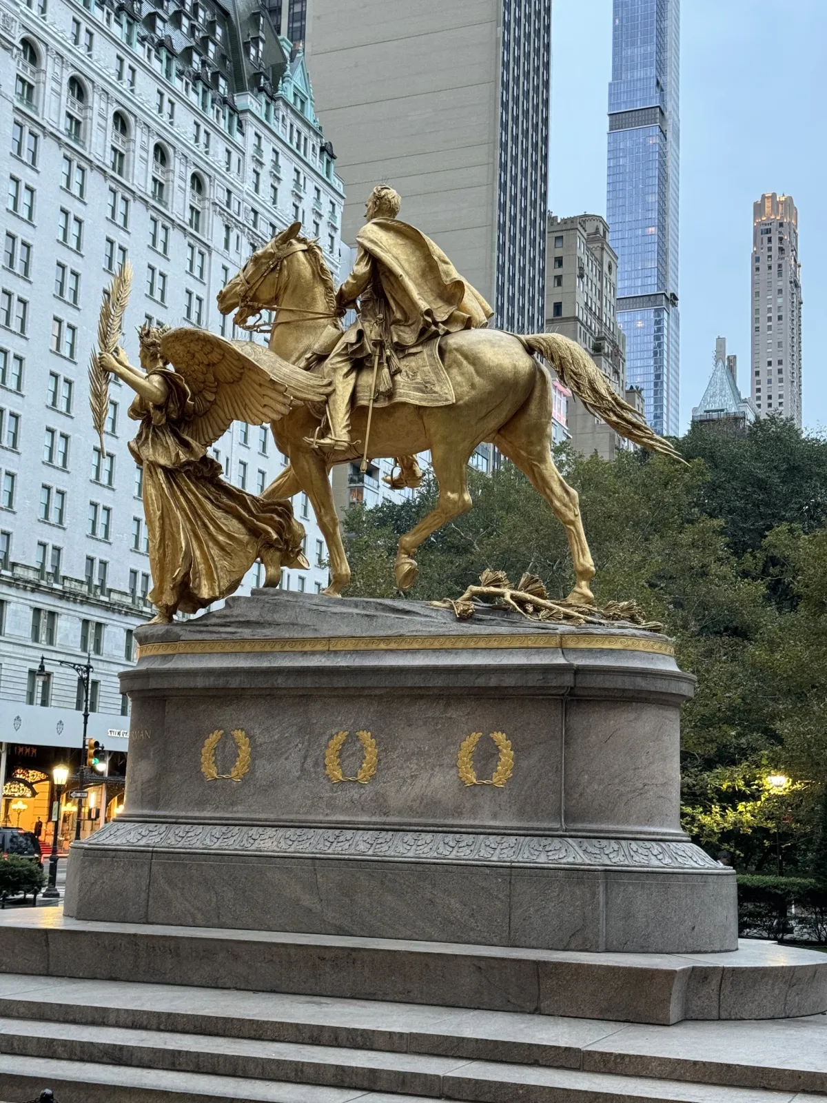 A gilded equestrian statue on a stone plinth, with buildings behind.