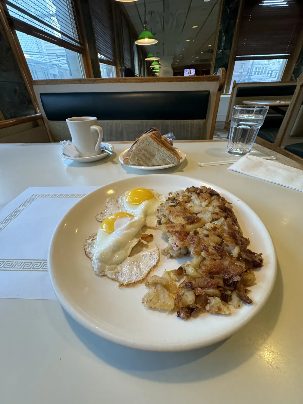A diner breakfast of fried eggs and hash browns, with coffee and toast on the table.