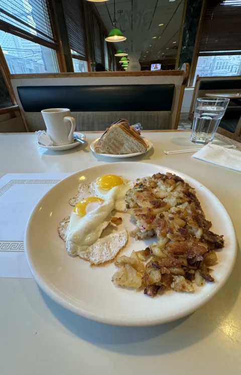 A diner breakfast of fried eggs and hash browns, with coffee and toast on the table.