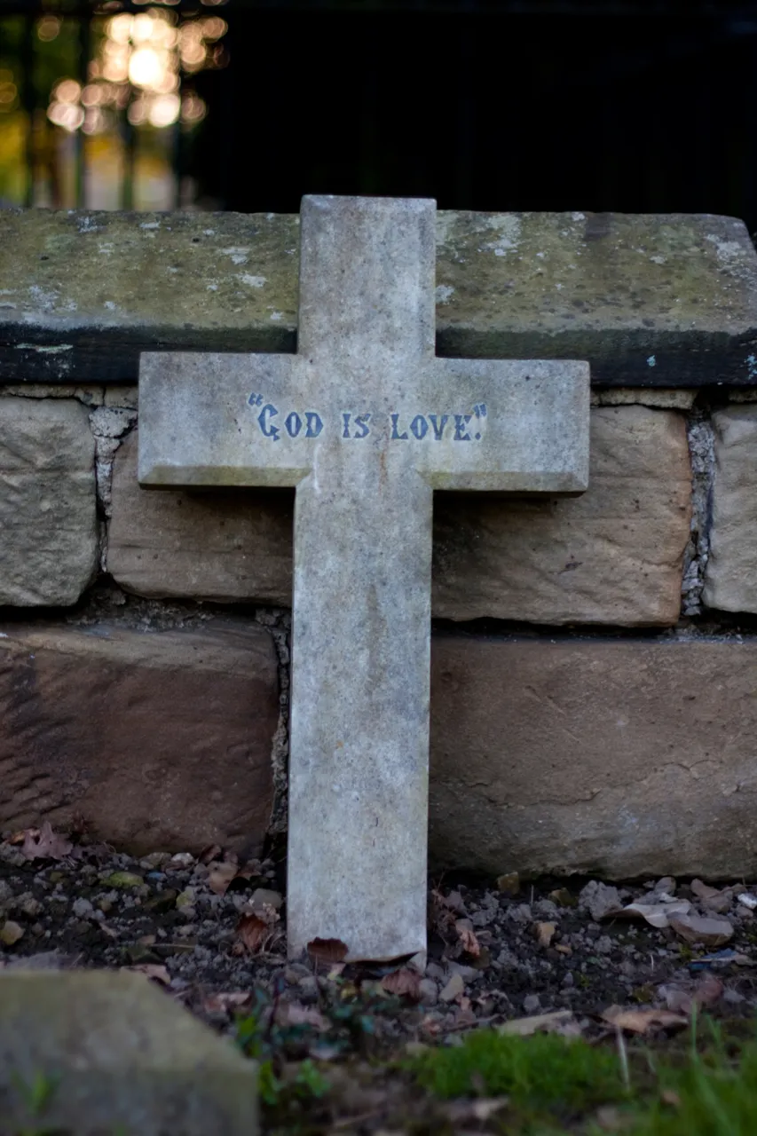 A weathered stone cross inscribed God Is Love, leaning against a wall.