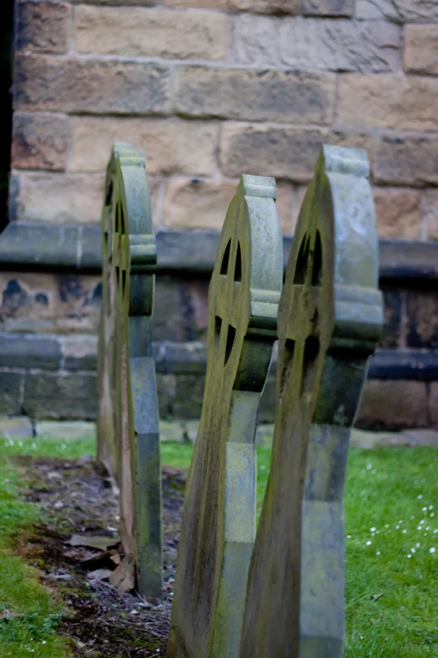Three leaning gravestones against a sandstone church wall.