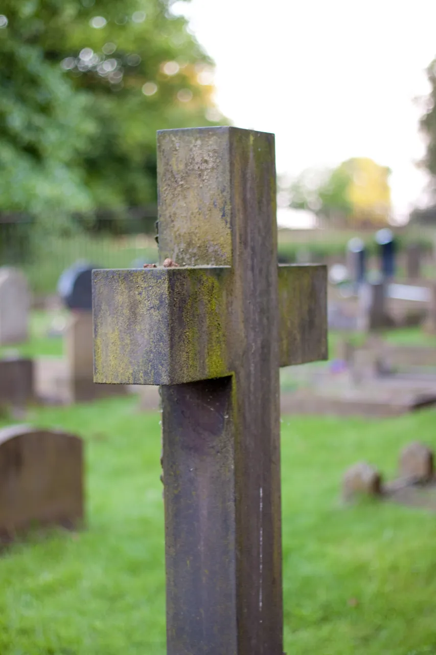 A lichen-covered wooden cross grave marker in a churchyard.