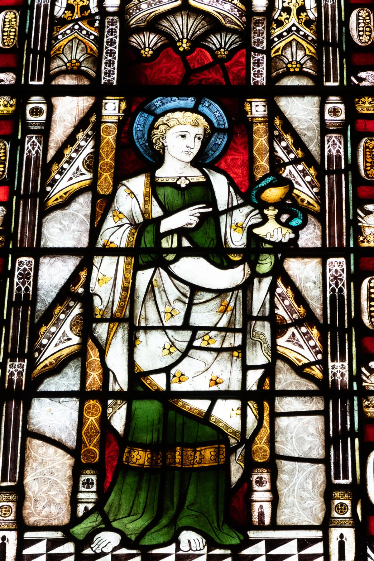 A stained-glass panel showing a haloed figure in green and white robes holding a cup.
