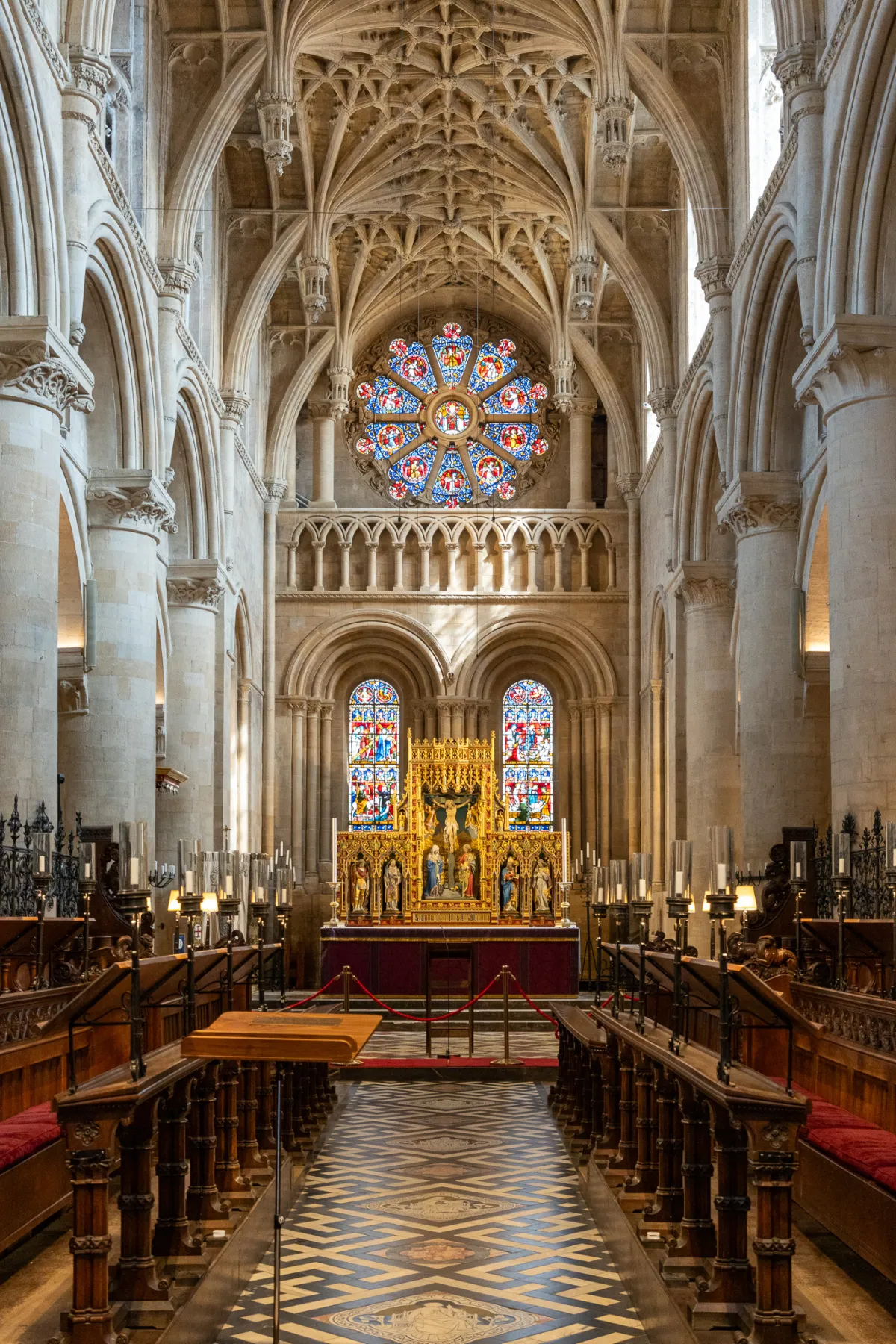 The interior of a cathedral looking towards a gilded altar, beneath a vaulted ceiling and rose window.
