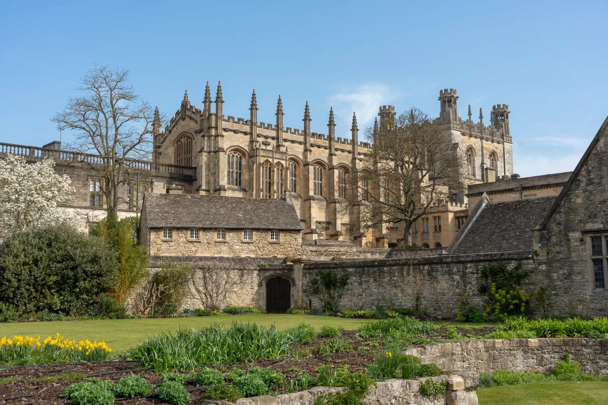 A pinnacled college chapel above a stone garden wall, with daffodils in the foreground.