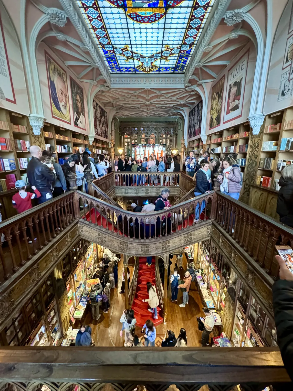 The interior of Livraria Lello, its stained-glass ceiling above two floors of crowded wooden book galleries.
