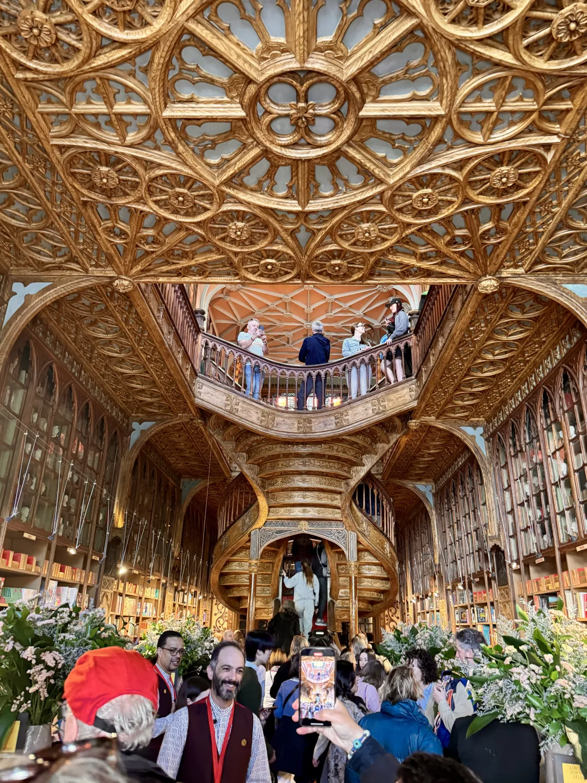 The carved ceiling and curving central staircase inside Livraria Lello, busy with visitors.