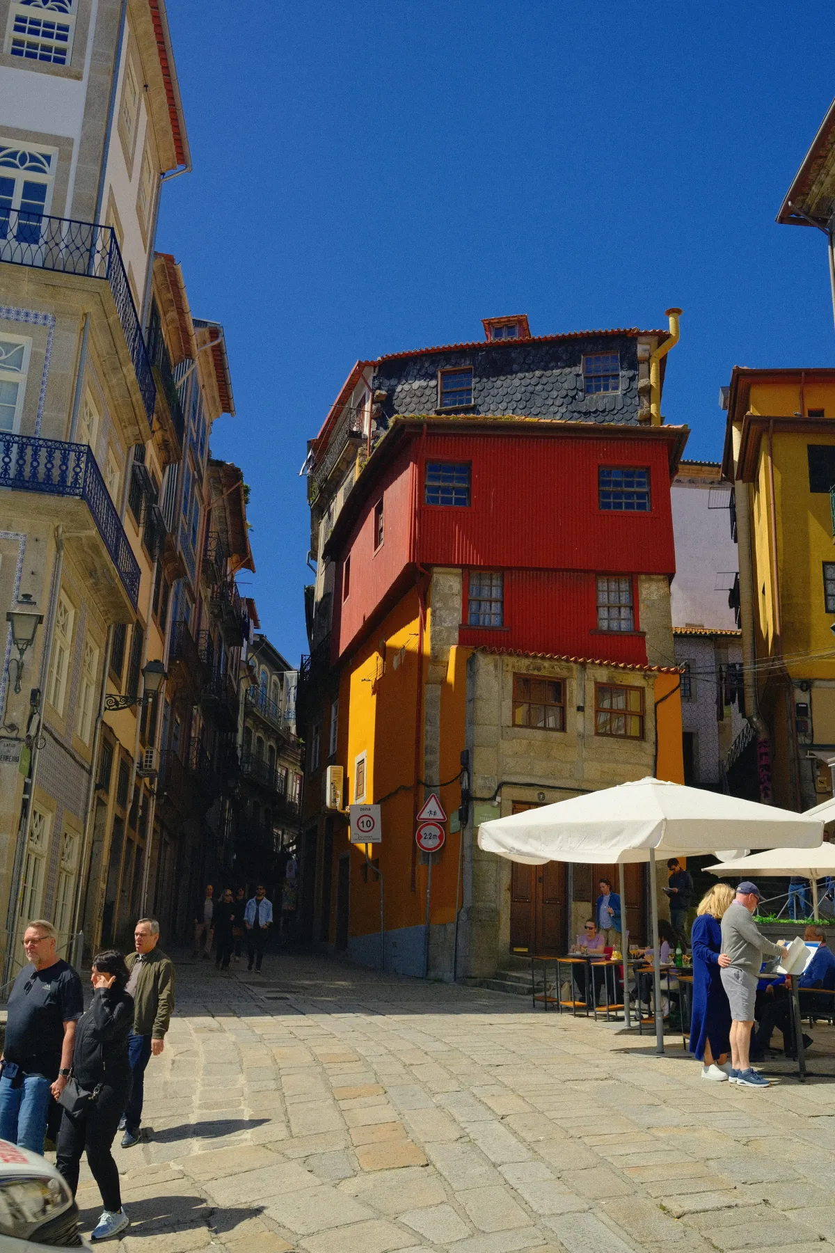 A tall red and ochre building on the corner of a cobbled square, with people walking past.