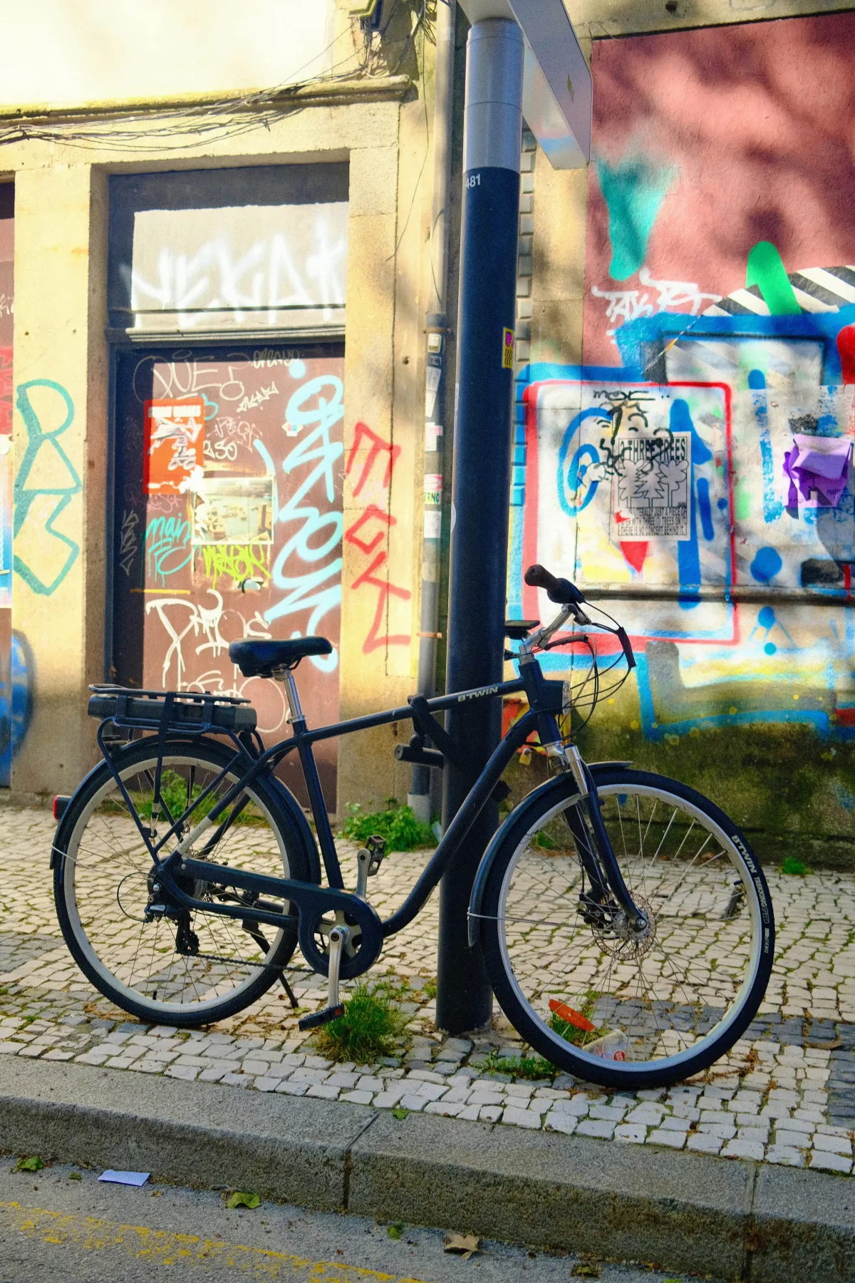 A bicycle propped against a lamp post in front of a heavily graffitied wall.