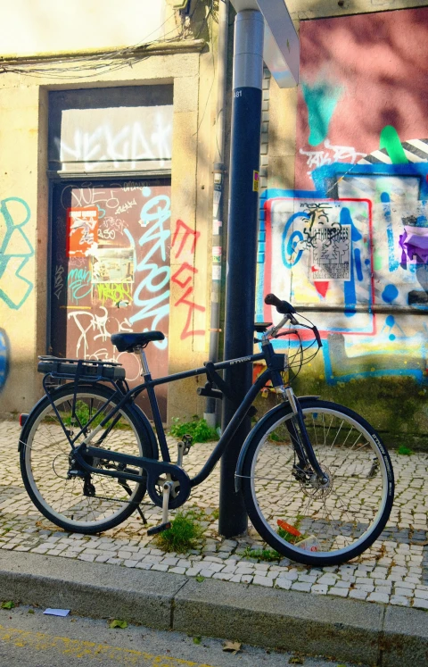A bicycle propped against a lamp post in front of a heavily graffitied wall.