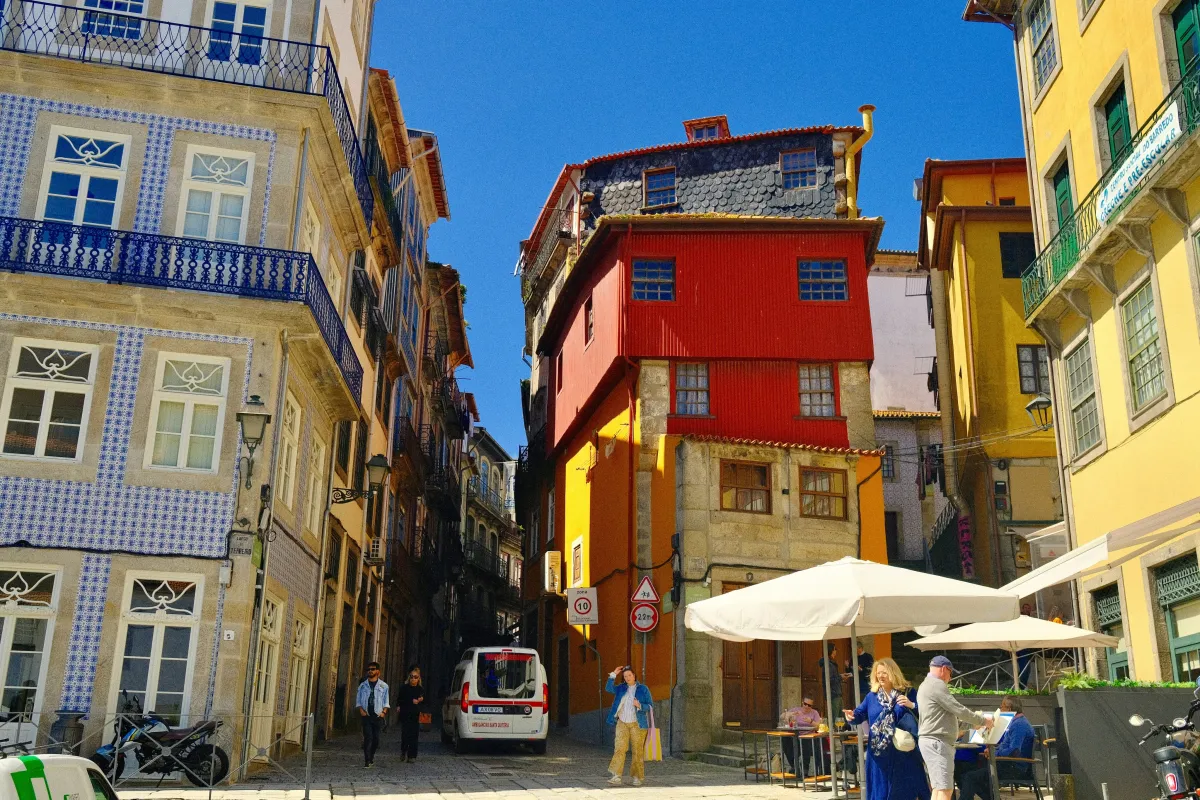 A red and yellow corner building on a small square, with café umbrellas set out below.