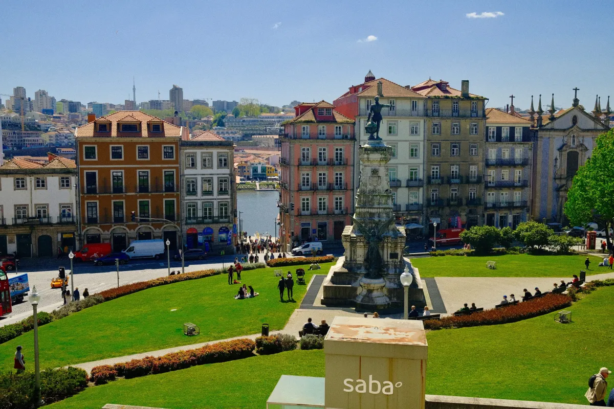 A stone monument at the centre of a formal garden square, with people sitting out on the grass.