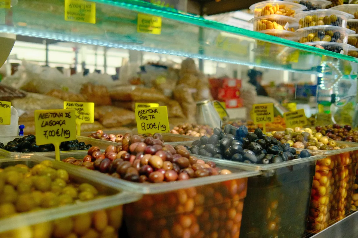 Trays of olives in a market display, each with a handwritten yellow price label.