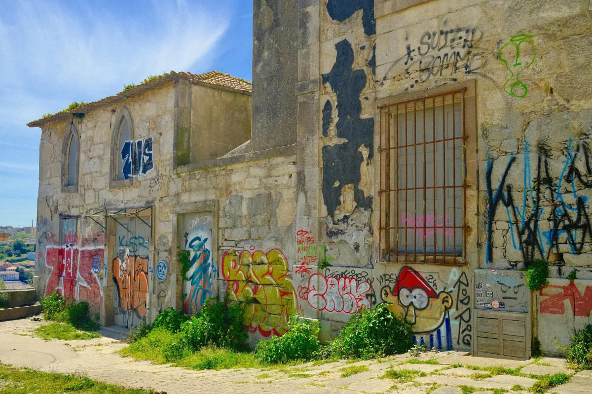 A derelict stone building covered in graffiti, its windows boarded and grass growing through the path in front.