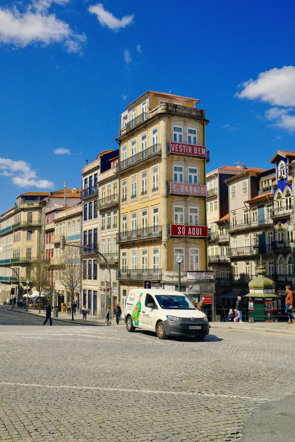 A tall corner building hung with painted advertising signs, above a cobbled square.