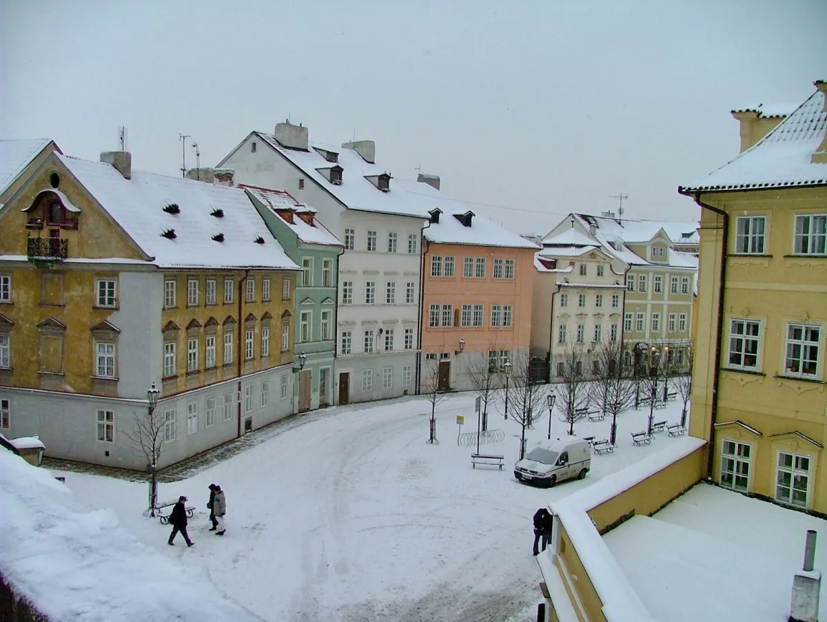 Pastel-coloured townhouses around a snow-covered square, with two people walking across it.
