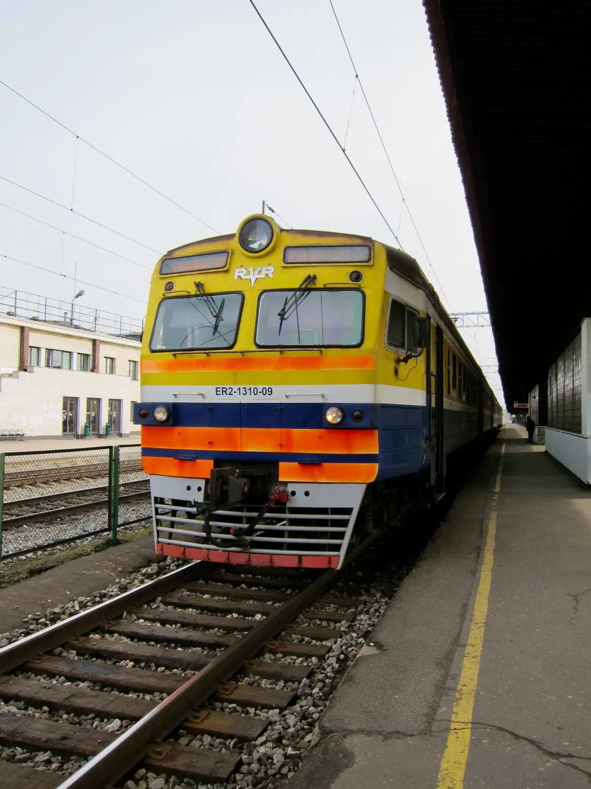 A yellow, orange and blue diesel train waiting at a station platform.