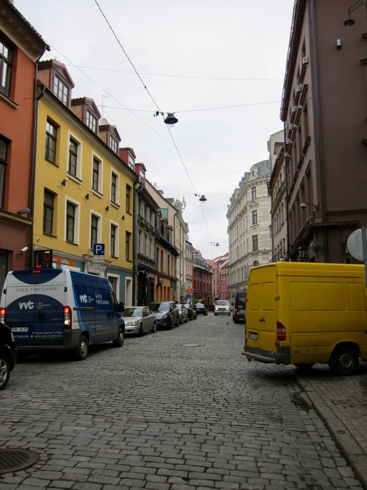 Vans and cars parked along a cobbled street lined with painted buildings.
