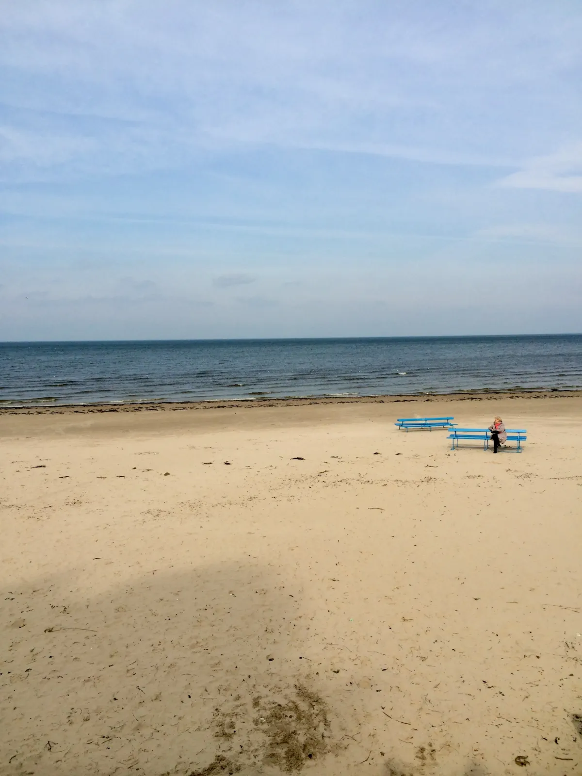 A near-empty sandy beach with a blue bench and a calm sea beyond.