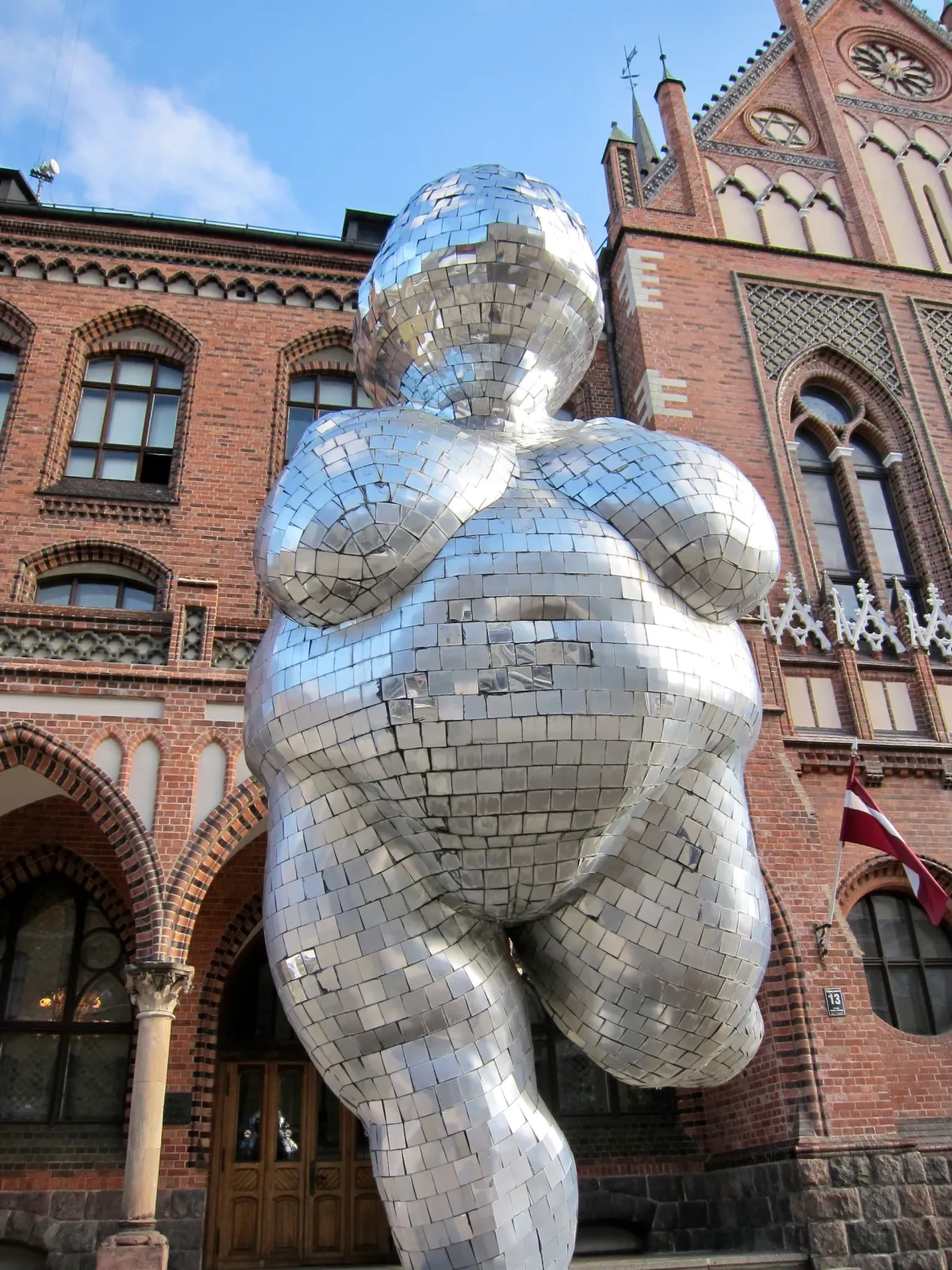 A large mirrored sculpture of a female figure outside a red brick building.