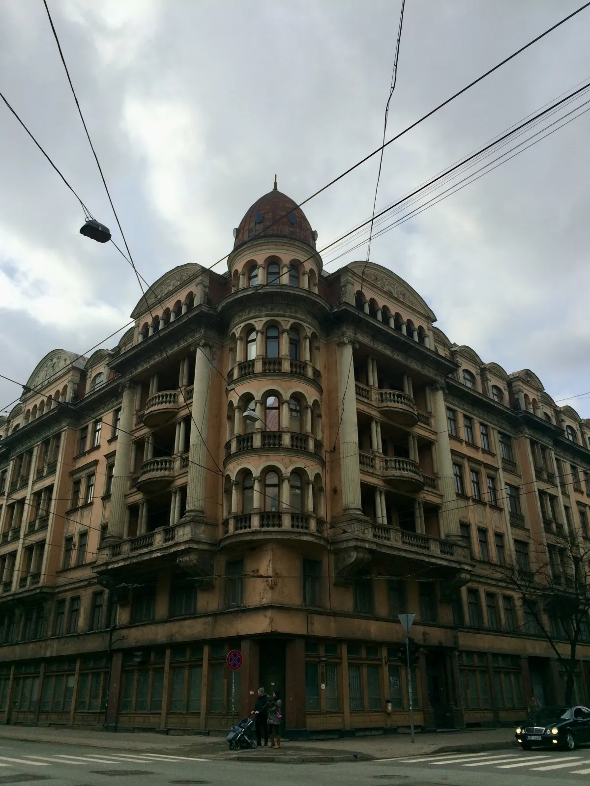 A large domed corner building with tiered balconies, seen from the street under grey sky.