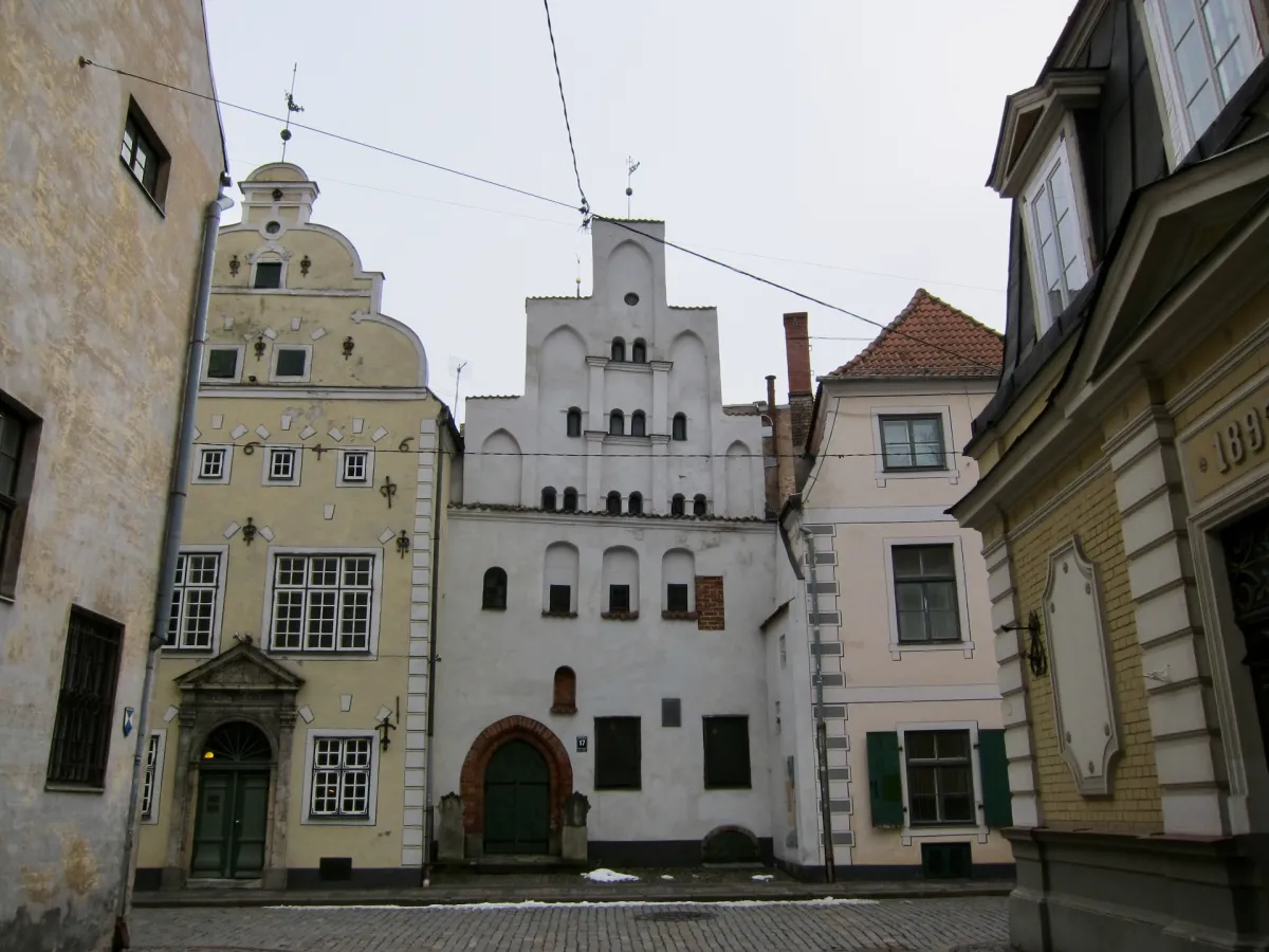Three adjoining gabled townhouses in cream, white and pink on a narrow street.