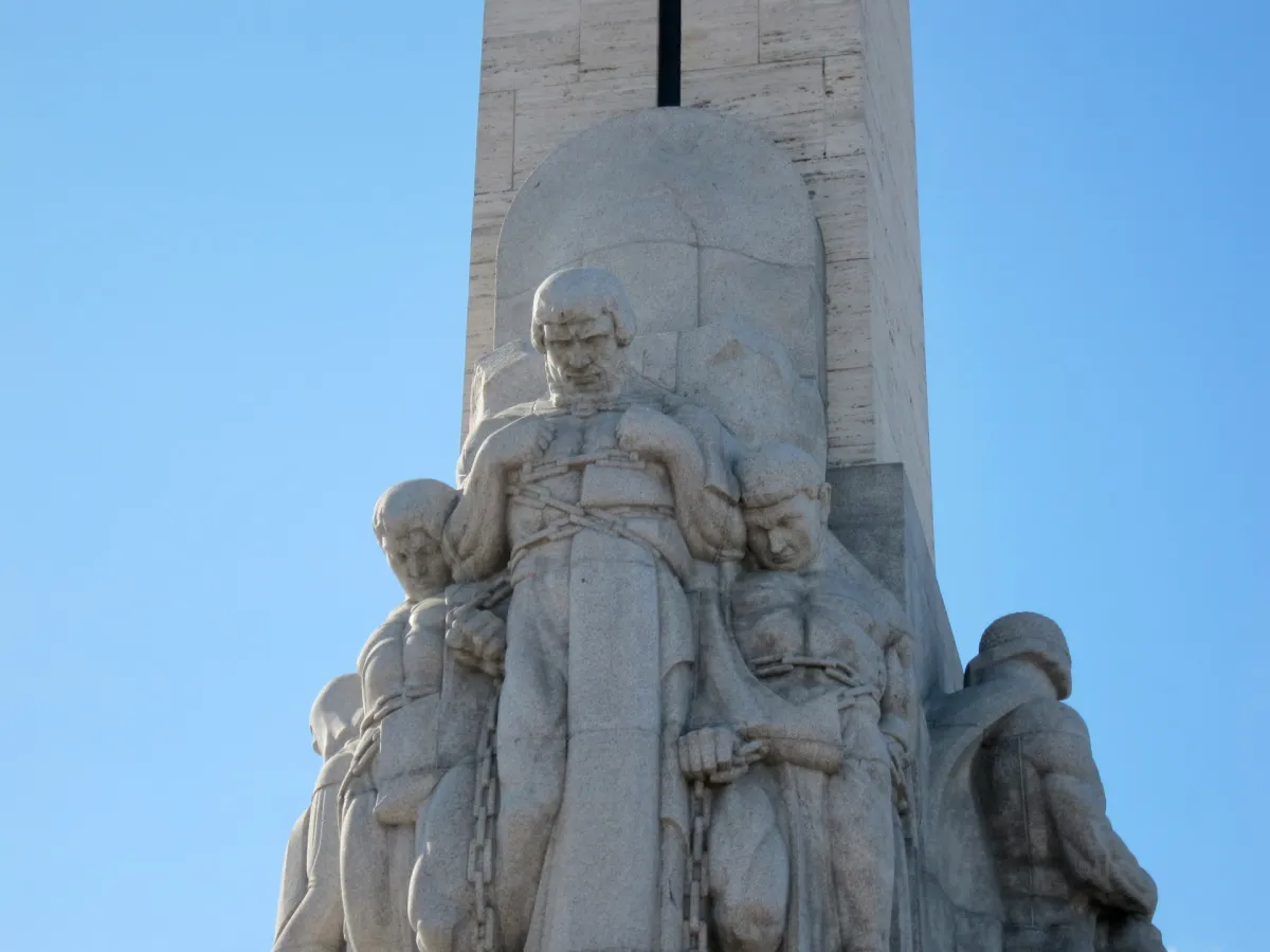 Carved stone figures at the base of a monument against a clear sky.