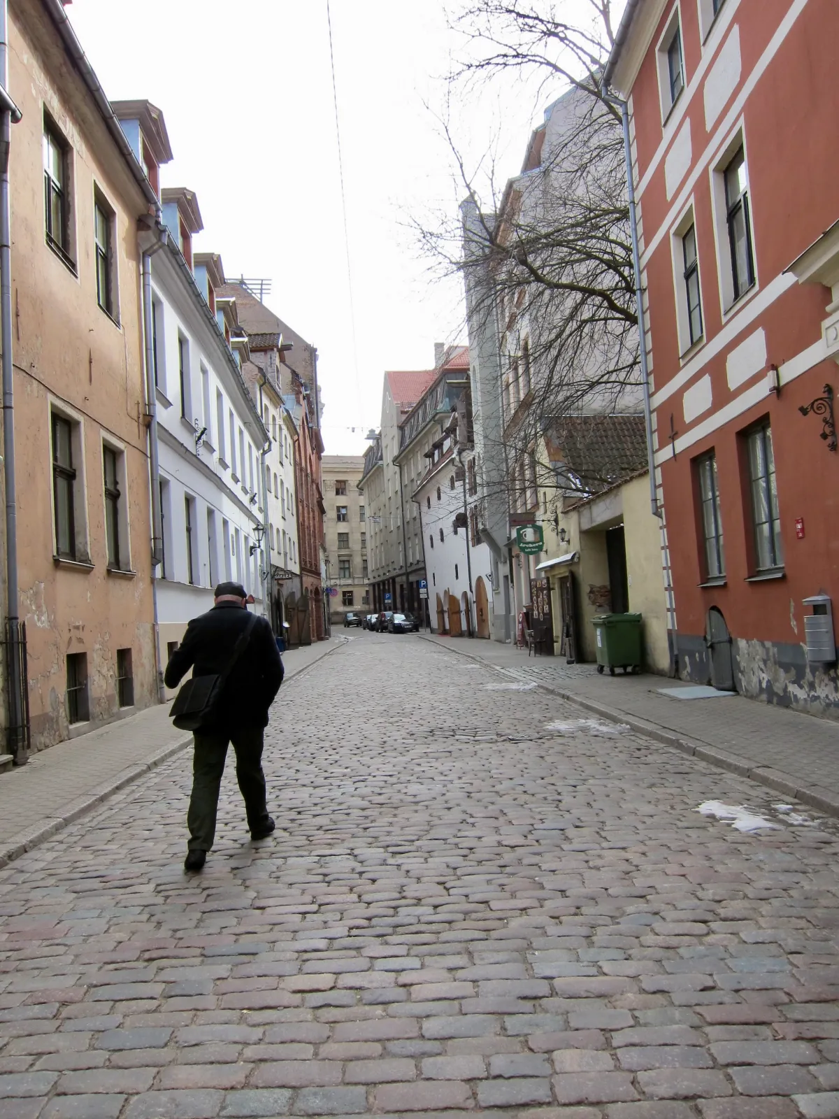 A man walking away down a wide cobbled street lined with old buildings.