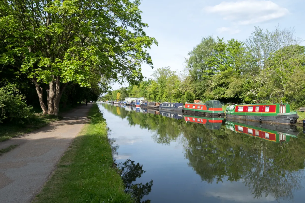 Narrowboats moored along a canal, with a towpath and trees on the opposite bank.