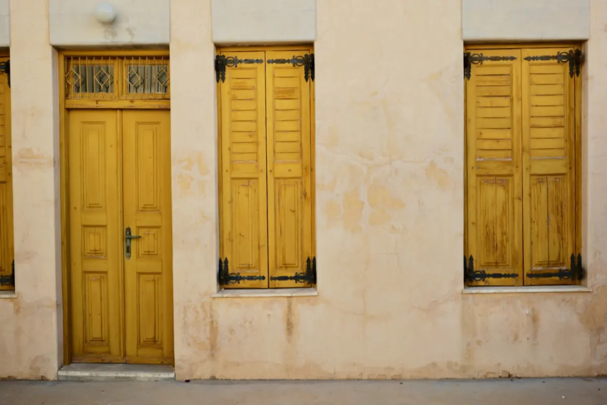 A yellow door and matching shutters on a pale rendered wall.