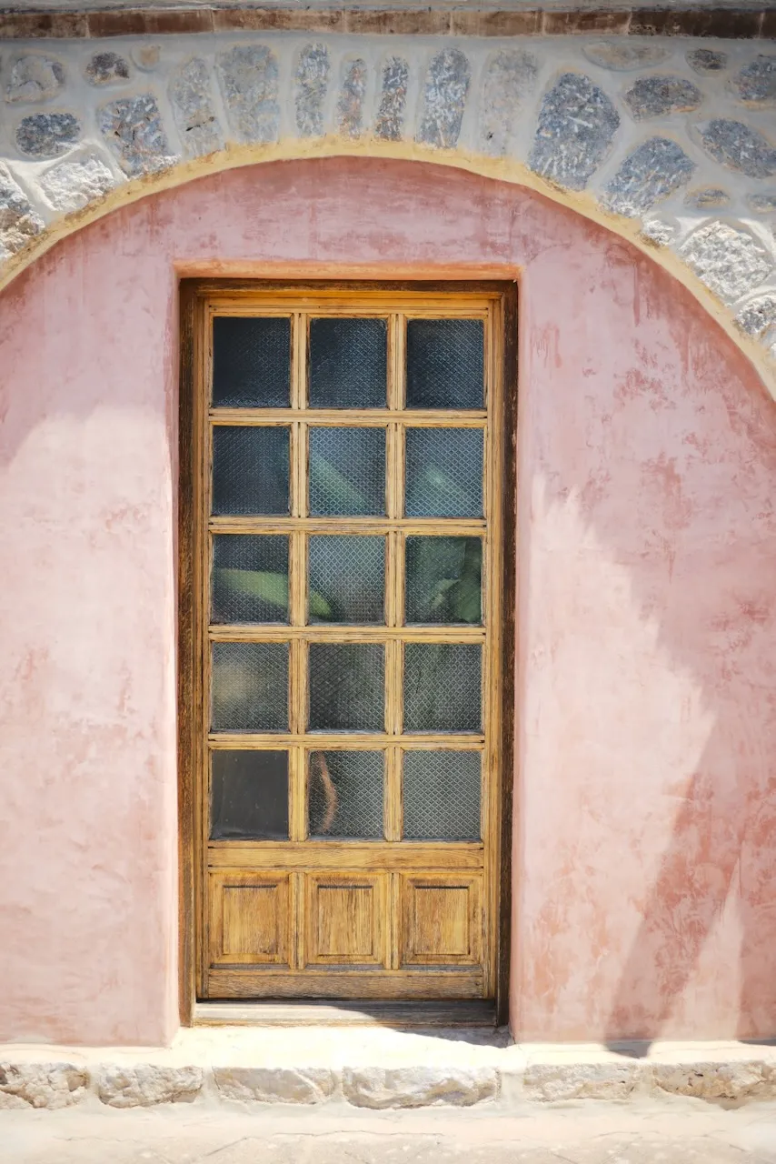 A glazed wooden door set in a pink arched doorway.