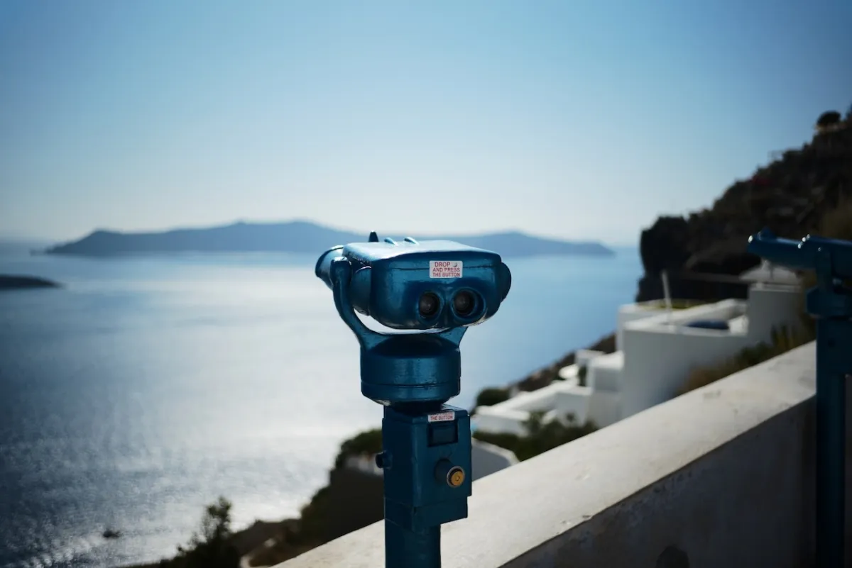 A coin-operated viewing telescope on a clifftop terrace above the sea.