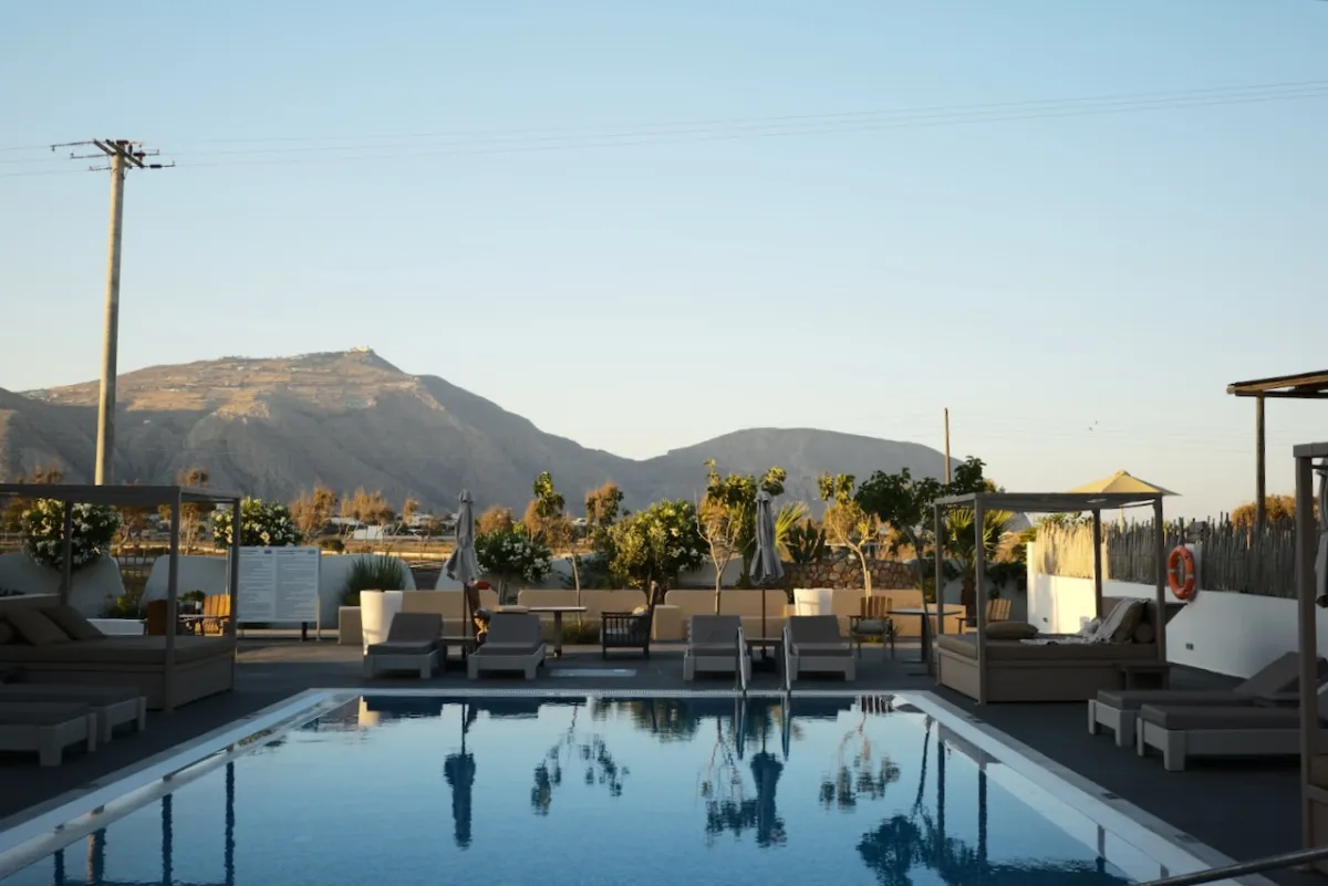 A hotel swimming pool with loungers, and hills behind at dusk.