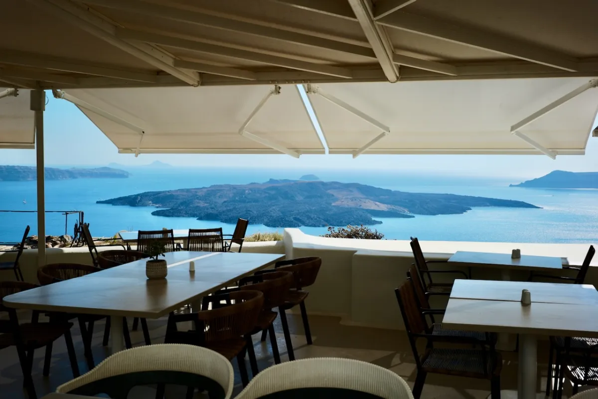 Tables under sun umbrellas at a clifftop restaurant, looking out over the caldera.