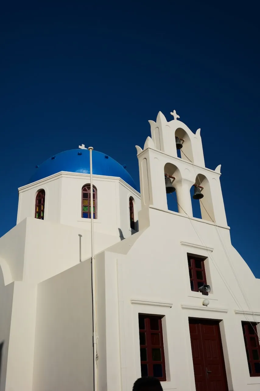 A white church with a blue dome and a three-bell tower against a deep blue sky.