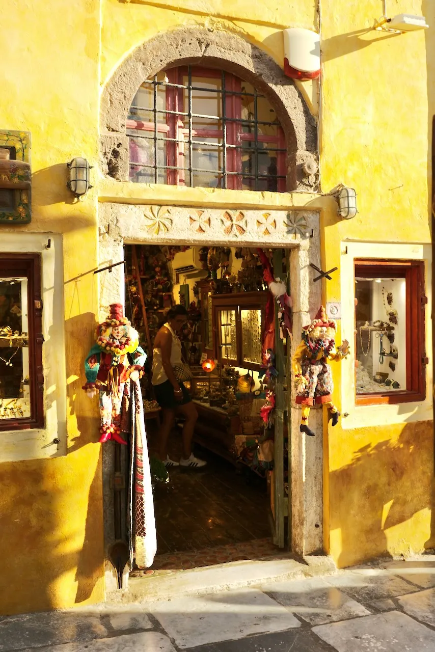 The open doorway of a souvenir shop in a yellow wall, hung with goods.