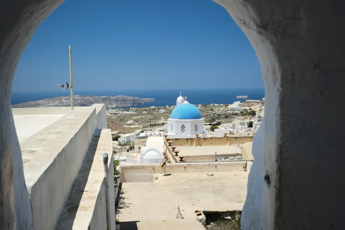 A blue-domed church seen through a whitewashed archway, with the sea beyond.