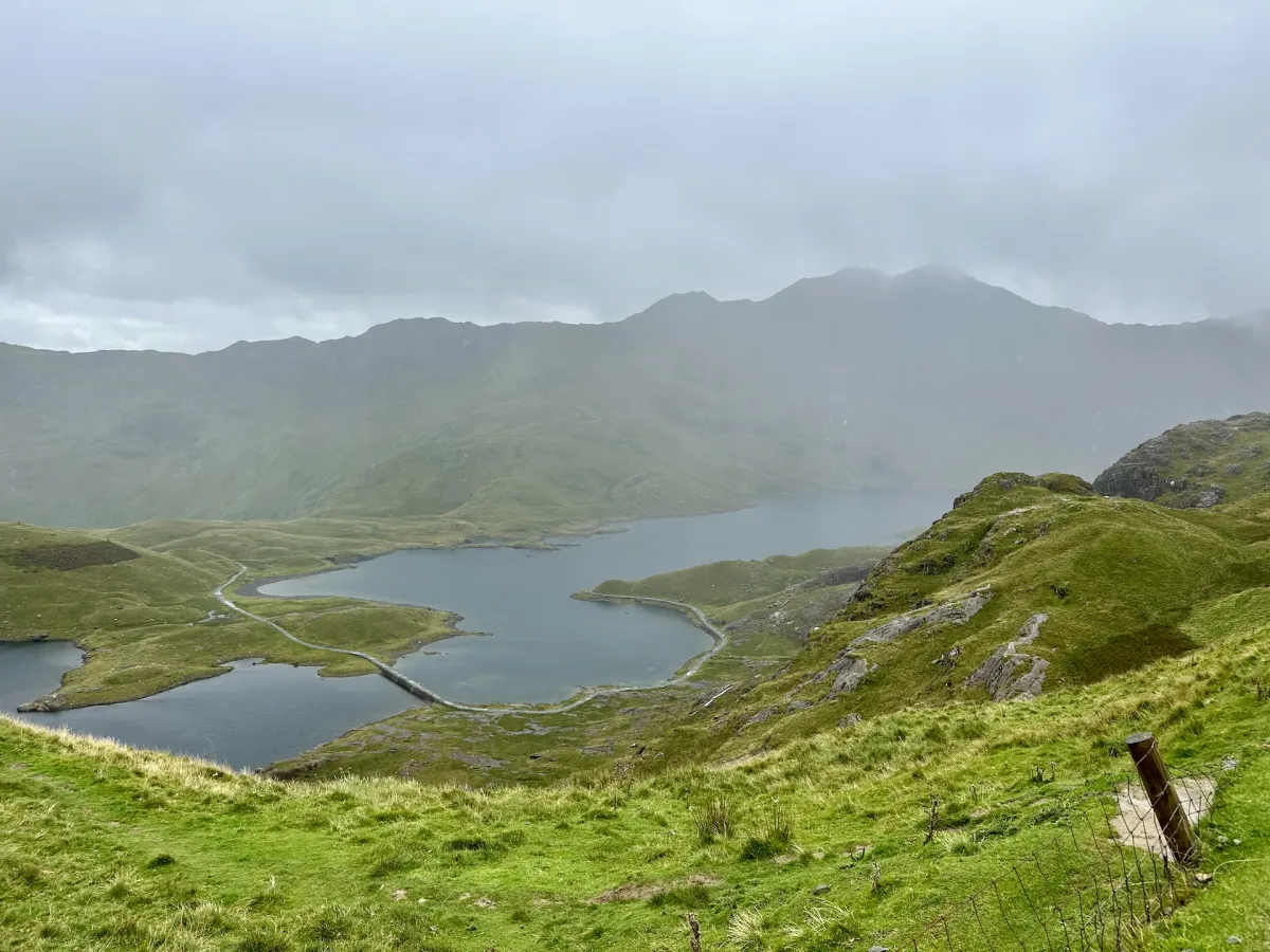 Two lakes on a green valley floor seen from above, with cloud covering the ridge behind.