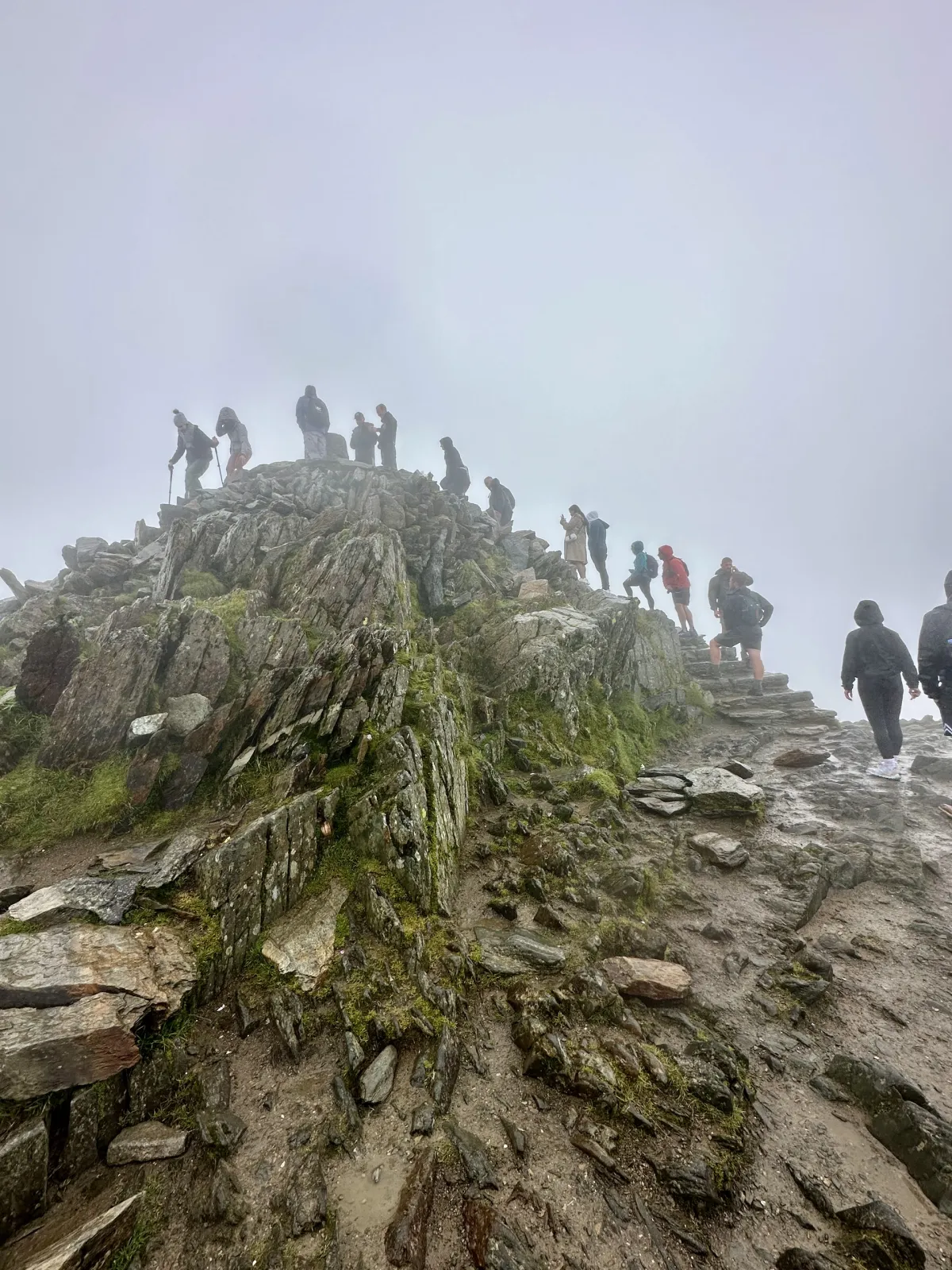 Walkers climbing the rocky summit path in thick cloud.