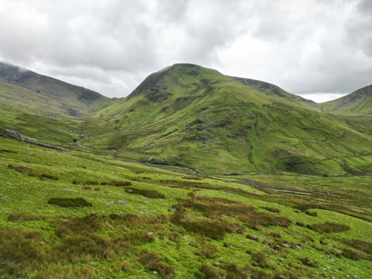 A green valley between steep hills under low cloud, with a path running along the floor.