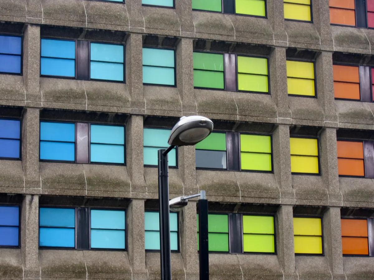 A grid of multicoloured window panels on a concrete facade, with a street lamp in front.