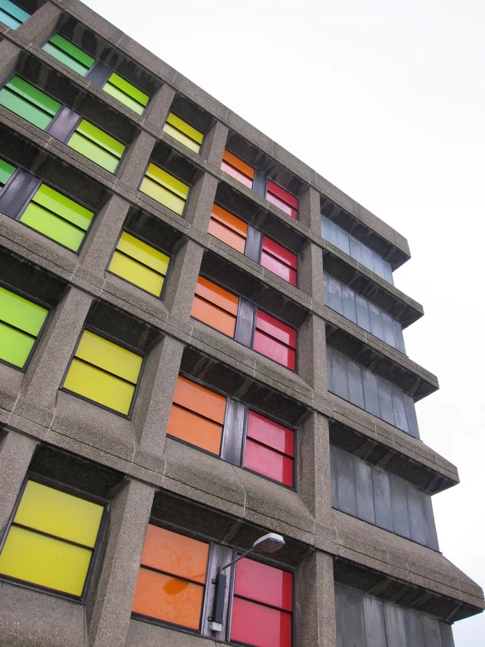 A concrete building faced with green, yellow, orange and red panels, seen from below.