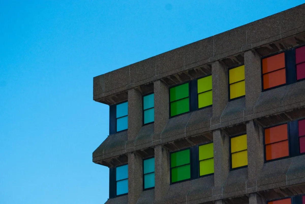The corner of a concrete building with panels of coloured glass, against a blue sky.