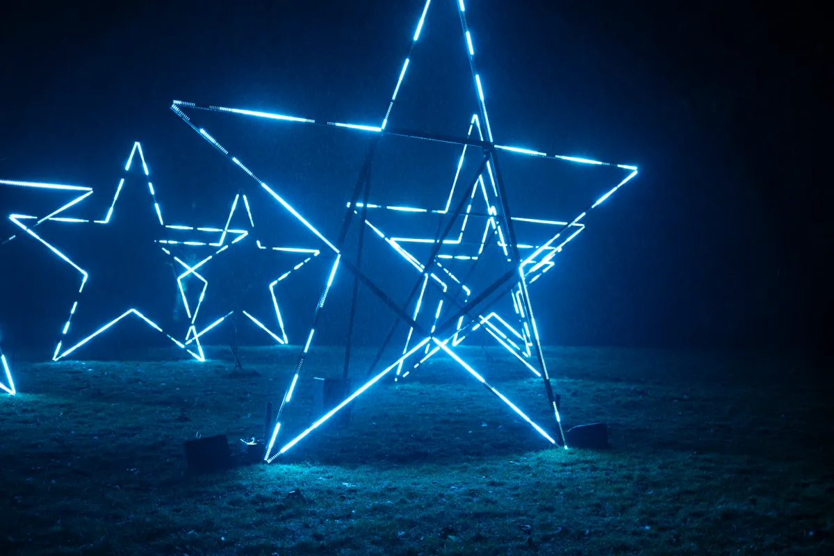 Illuminated star frames lit in blue on a lawn at night.