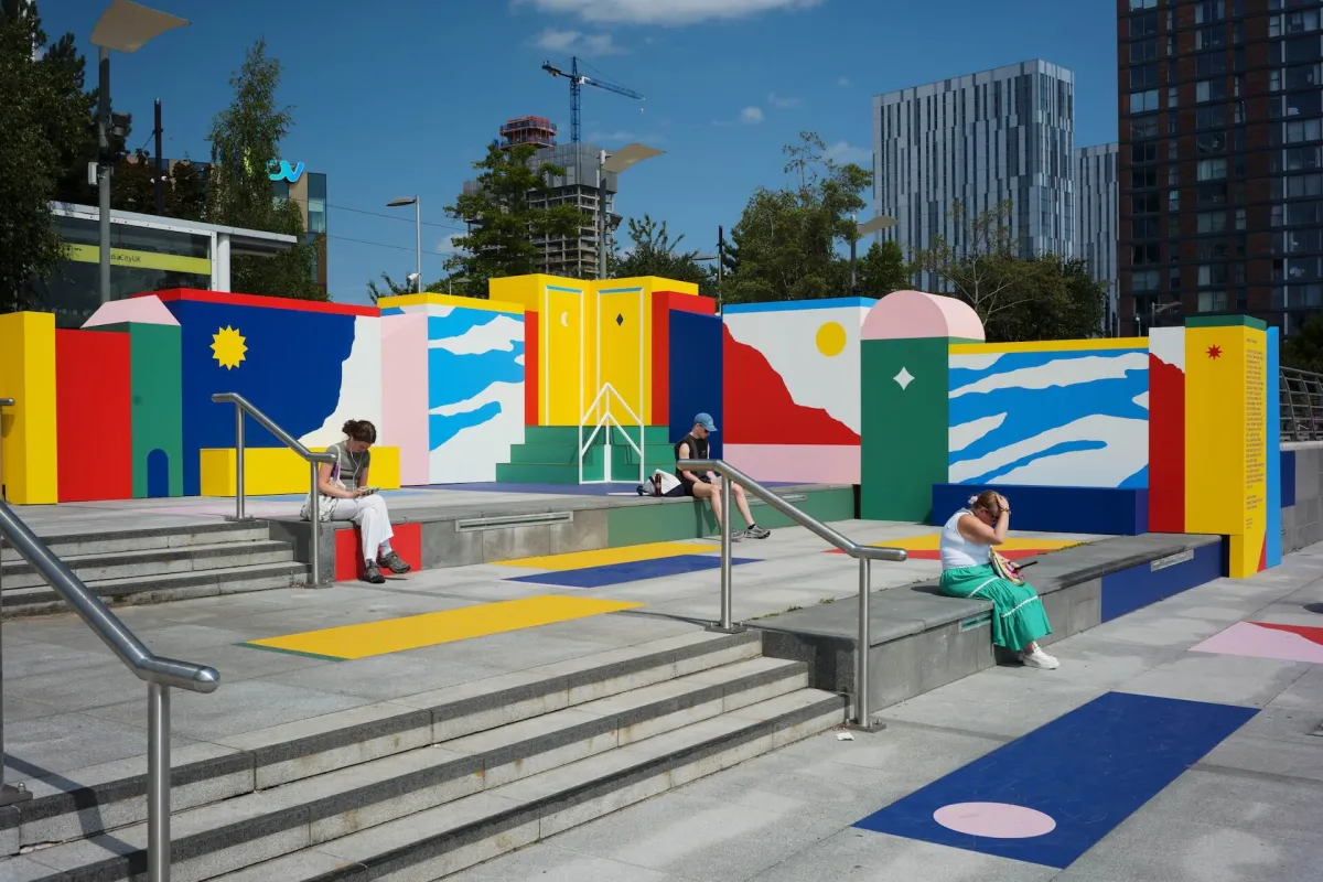People sitting on steps in front of a brightly painted mural wall.