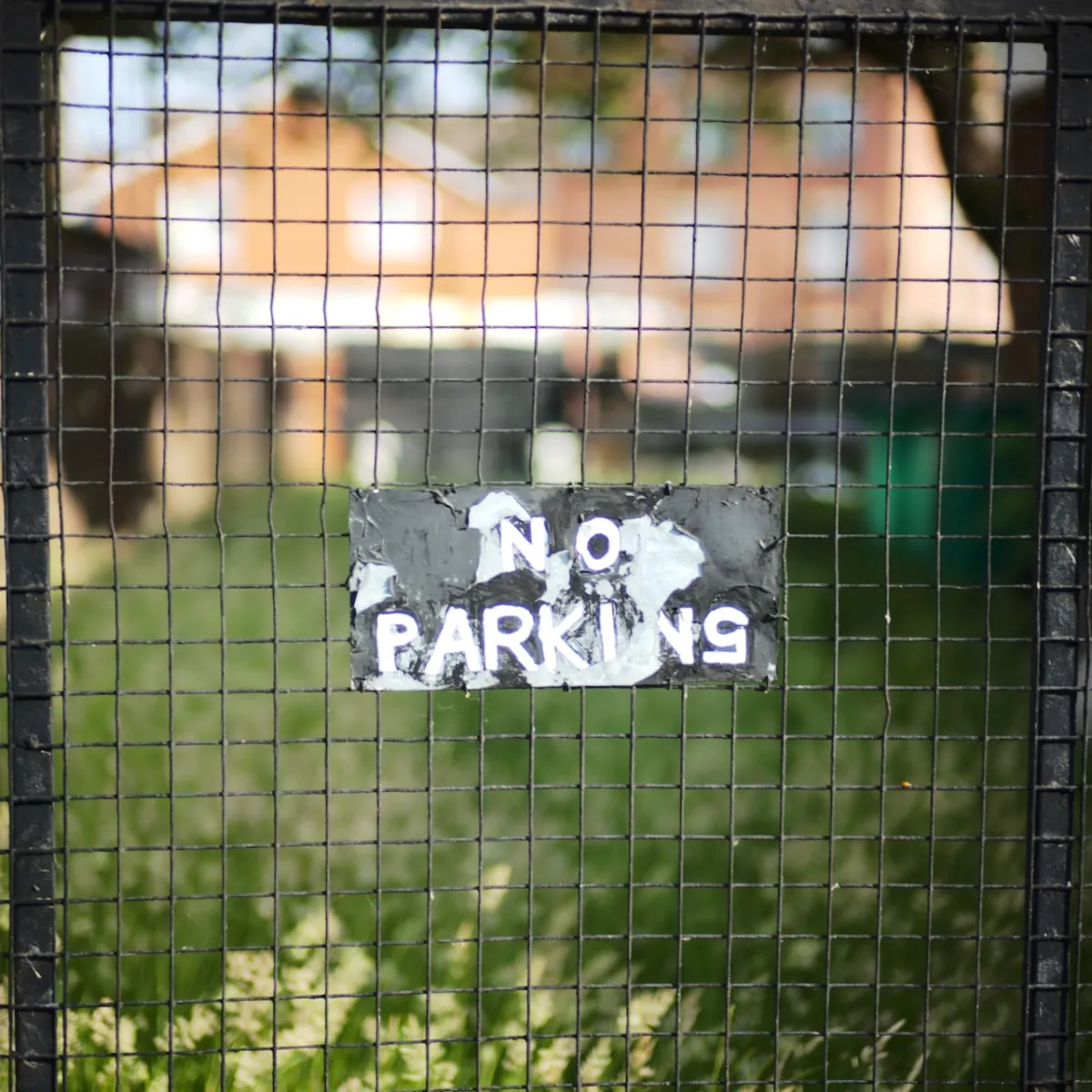 A hand-painted No Parking sign fixed to a wire mesh fence.