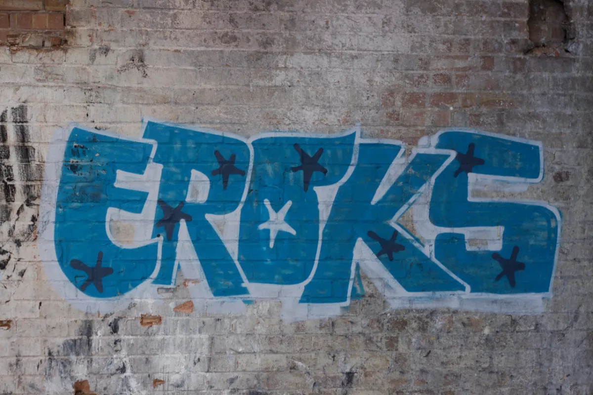 Blue block lettering reading Eroks, painted on a whitewashed brick wall.