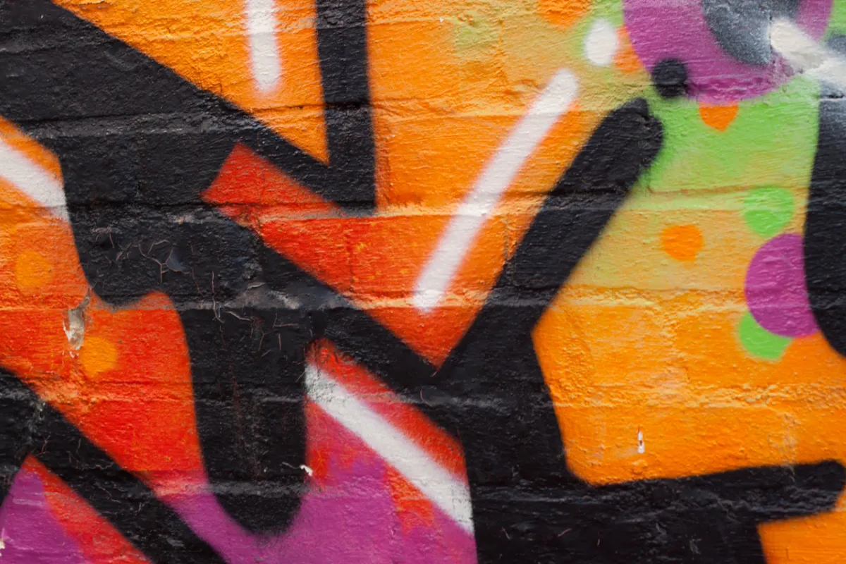 Close-up of orange, black and purple spray-painted lettering on brickwork.